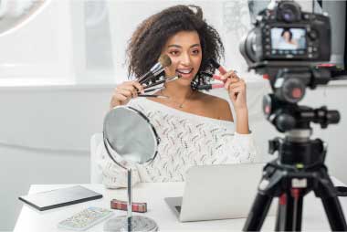 Happy Lebanese Influencer with Braces Holding Lip Glosses – VYB STUDIOS Beauty Content Shoot Selective focus on a smiling Lebanese influencer with braces holding lip glosses and cosmetics during a beauty product shoot.