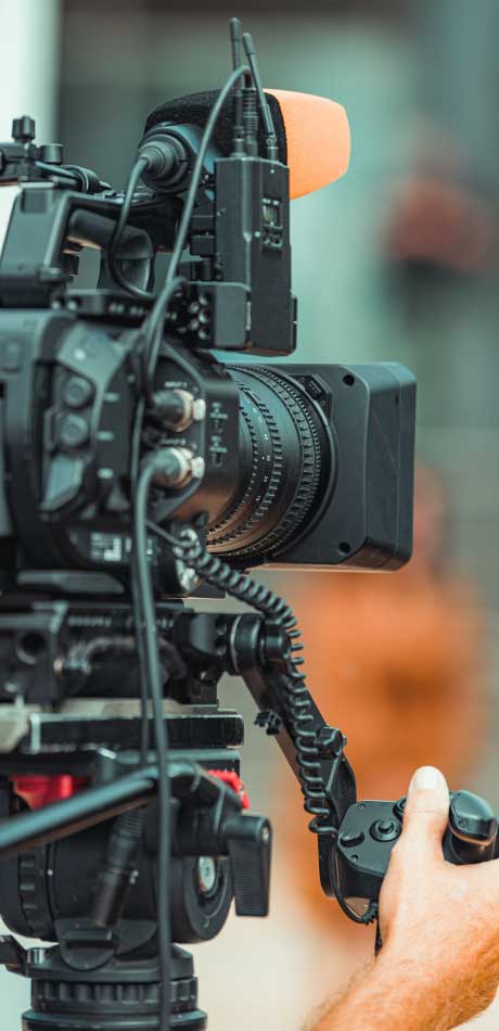 Professional TV camera filming a publicity event with audience and speakers in view.