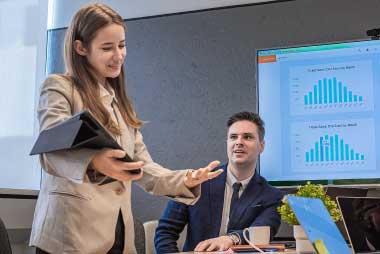 Team meeting with charts on a large screen in the background and iPads in hand, analyzing live event and social content performance metrics.